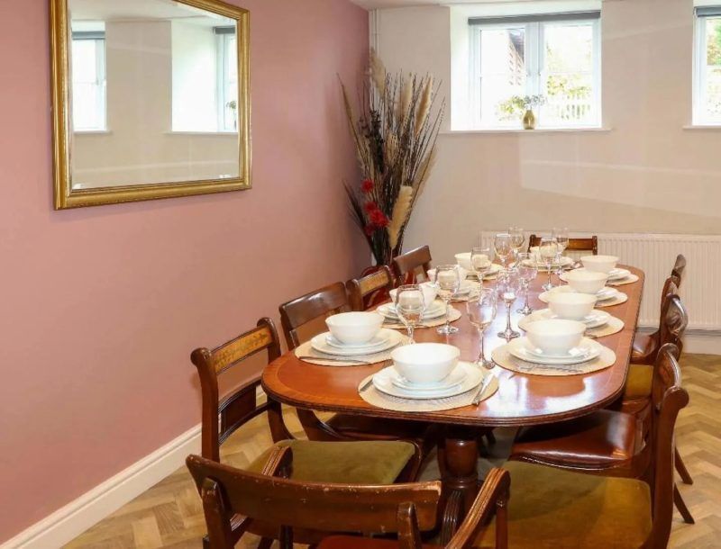 Dining room with an oval table set for a meal; chairs surround the table, a mirror hangs on the wall.