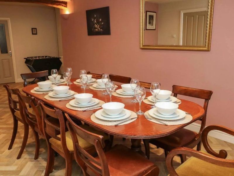 Formal dining table set for a meal. Includes wooden table, chairs, place settings, and a mirror.