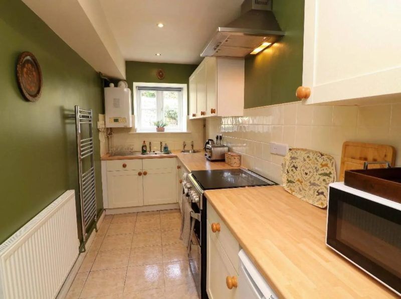 Kitchen with olive green walls, white cabinets, and wooden countertops.