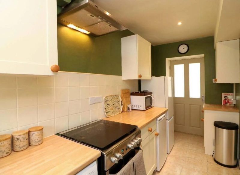 A small kitchen with light-colored cabinets, a stove, and a door leading outside. Green wall.