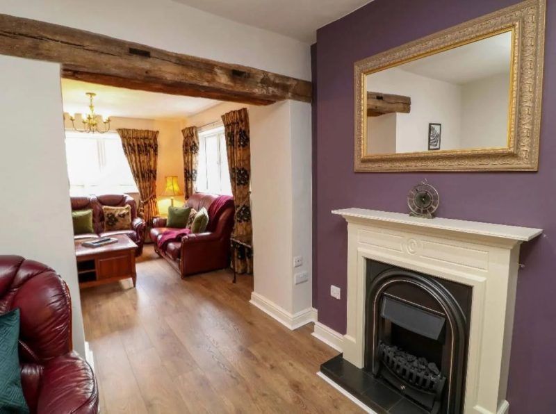 Living room interior with purple wall, fireplace, mirror, and a view into the adjacent room.