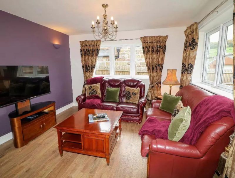 Living room with red leather furniture, purple wall, chandelier, and wood coffee table.