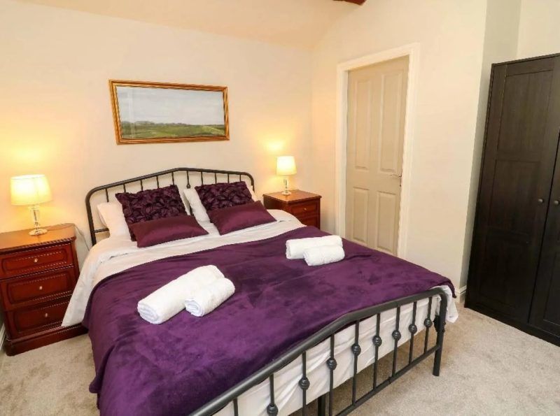 Bedroom with black metal bed frame, purple bedding, nightstands, and dark wardrobe.