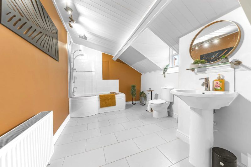 Modern bathroom with white tiling, a bathtub, and an orange accent wall.