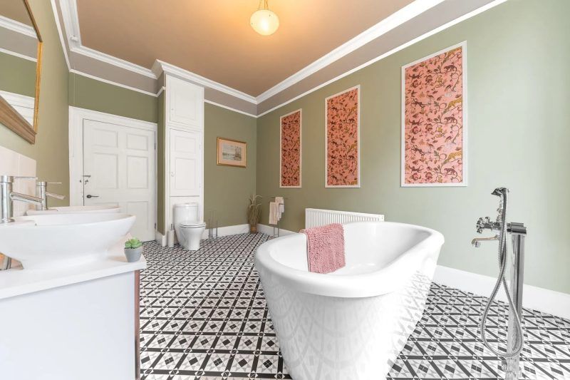 Bathroom with clawfoot tub, patterned tile floor, olive green walls, and three framed pink art pieces.