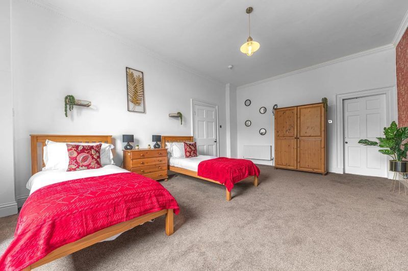 Bedroom with two twin beds, red bedding, wooden furniture, and decorative accents.