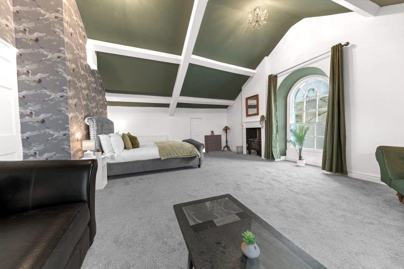 Spacious bedroom with a bed, sofa, large window, and green and grey color scheme.