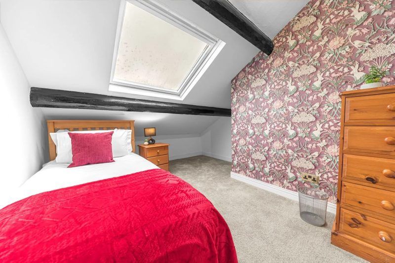 Bedroom with a single bed, skylight, floral wallpaper, and wooden dresser.