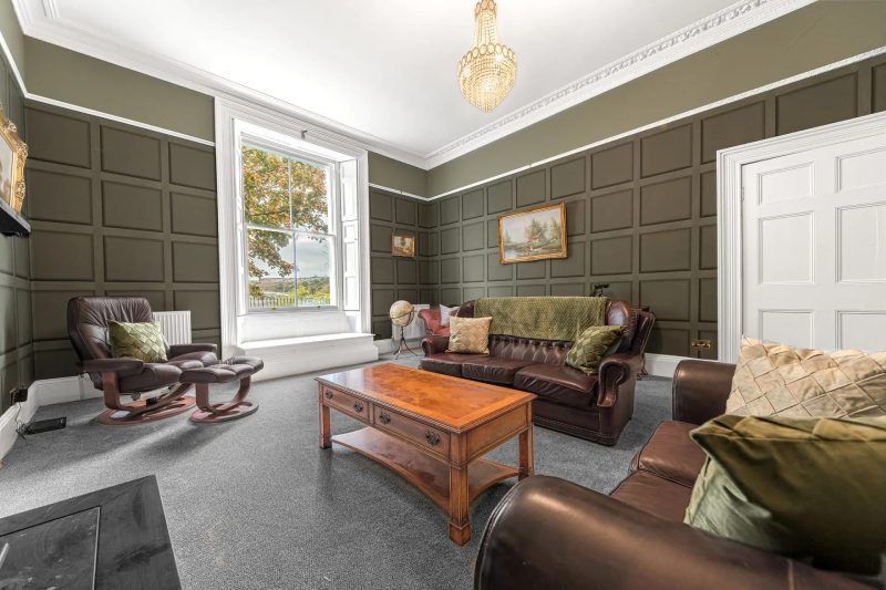 Living room with dark green paneling, leather furniture, and a large window.