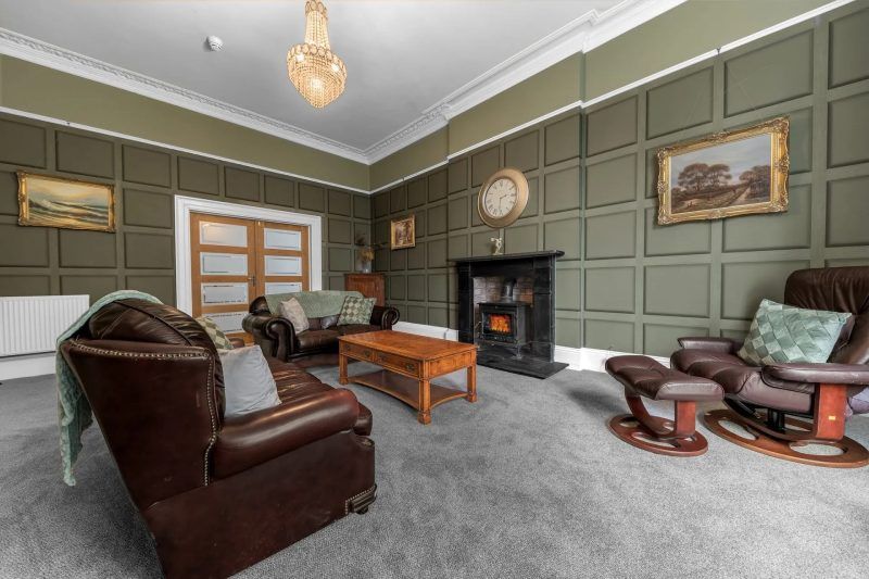 Living room with olive green paneled walls, fireplace, and leather furniture.