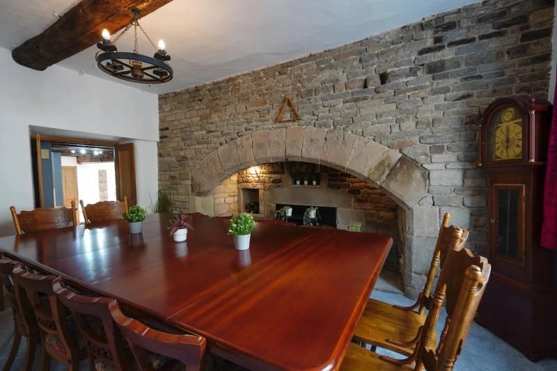 Dining room with large wooden table, stone fireplace, and grandfather clock.