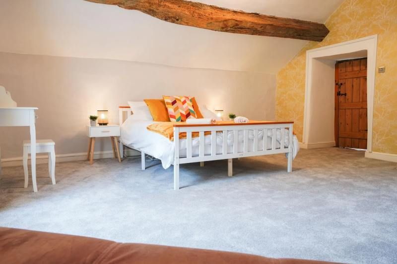 Bedroom with white bed, beige walls, wooden beams, and a wooden door.