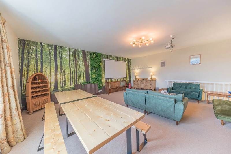 Room with forest mural, long wooden tables, sofas, and a projection screen.