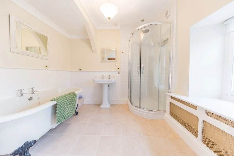 Bathroom with claw-foot tub, shower, pedestal sink, and window with radiator, beige and white.