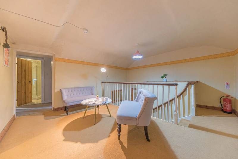 A bright, second-floor landing with two light pink chairs, a small table, and a staircase.