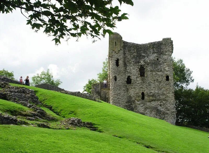 Ruined stone castle tower on a green grassy hill under a cloudy sky.