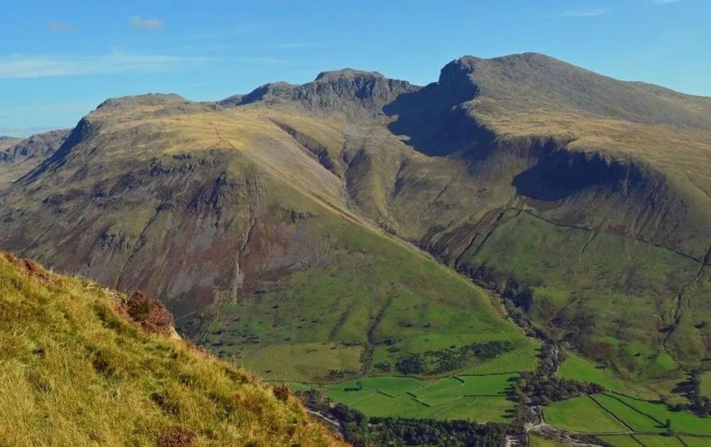 Mountain landscape with green and brown slopes under a blue sky.
