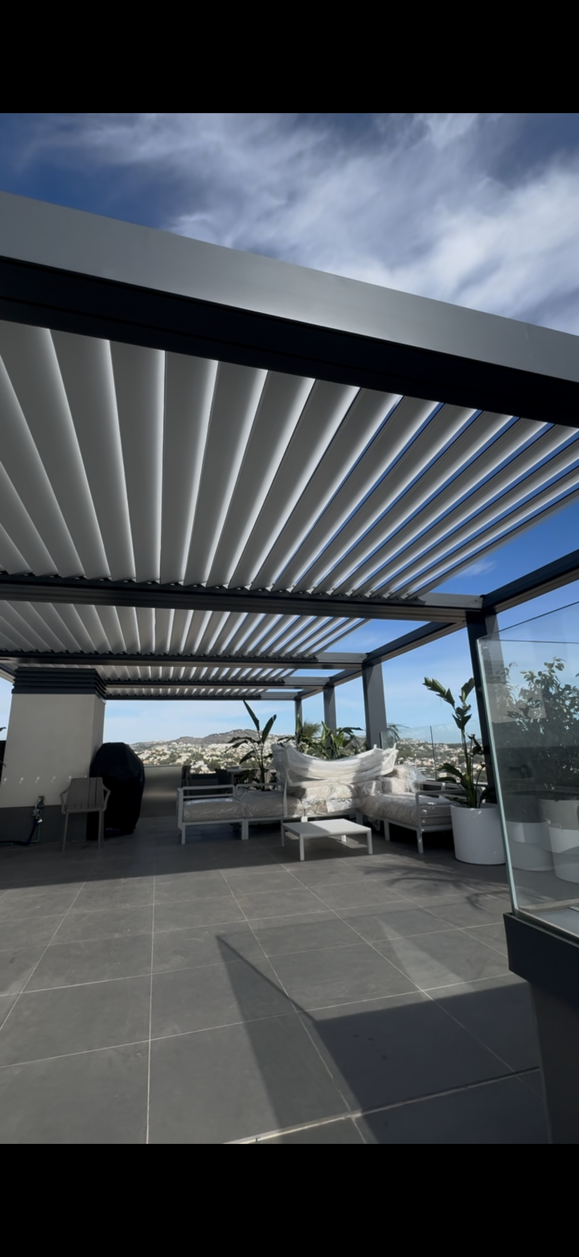 Patio al aire libre con techo retráctil y asientos, con vista al horizonte de la ciudad bajo un cielo azul.