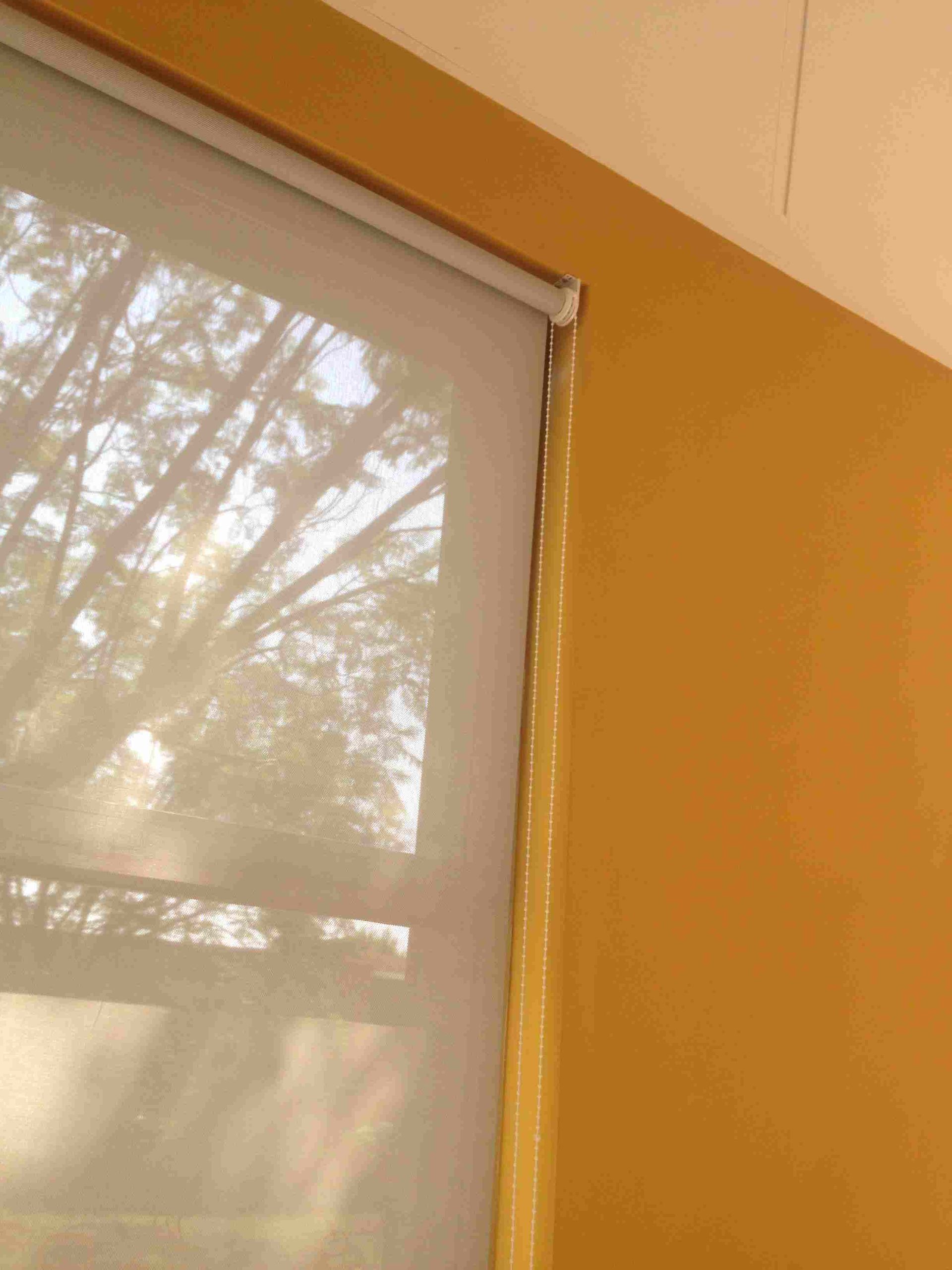 Una ventana con una persiana y una pared amarilla.