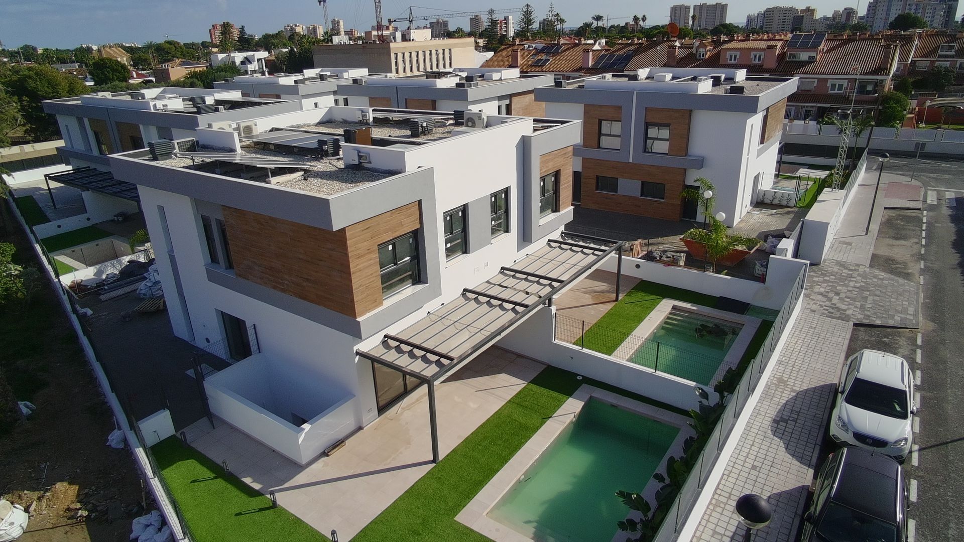 Modernas casas adosadas con piscinas y patios; día soleado.