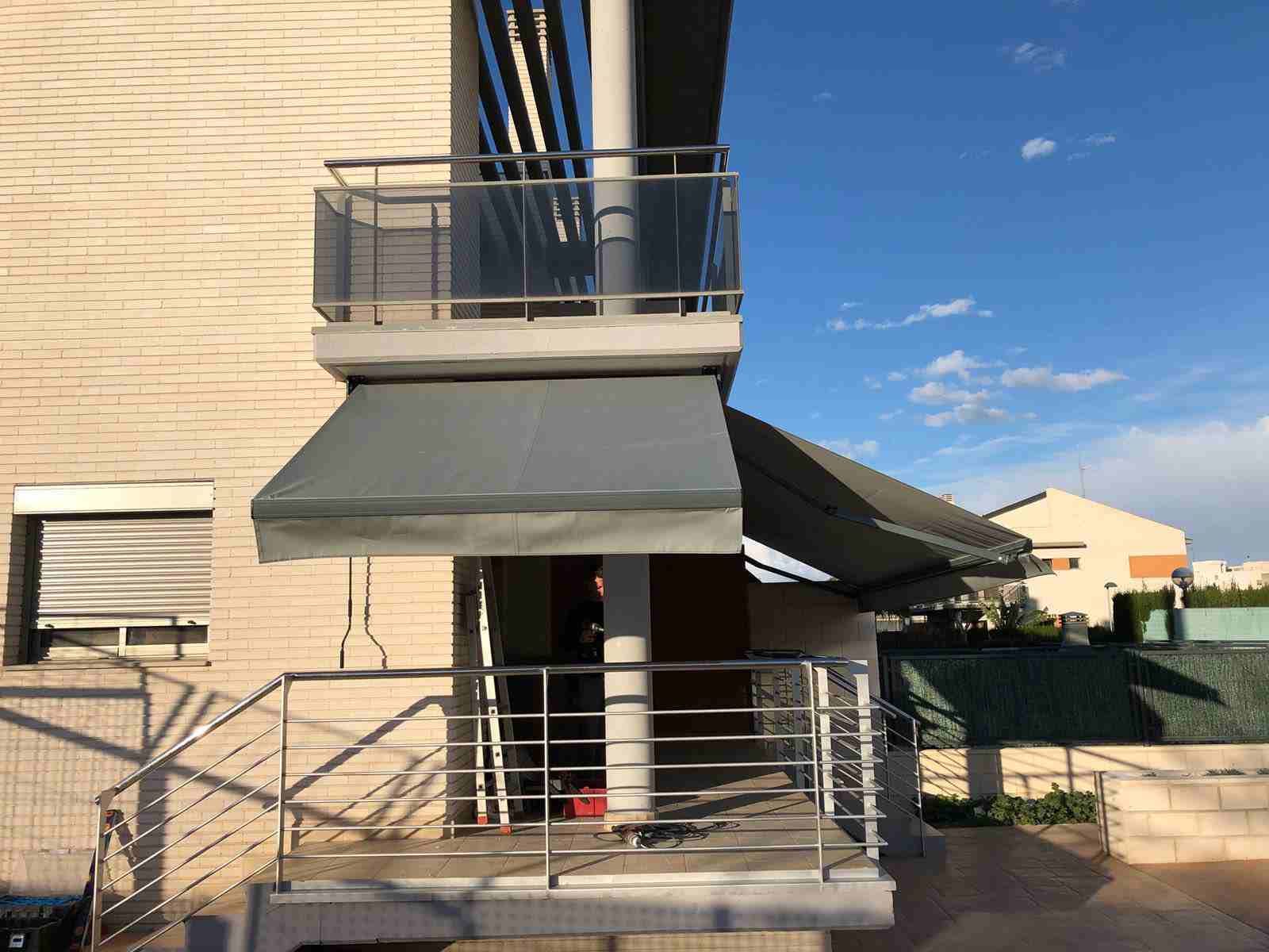 Un balcón con toldo gris y barandilla de acero inoxidable.