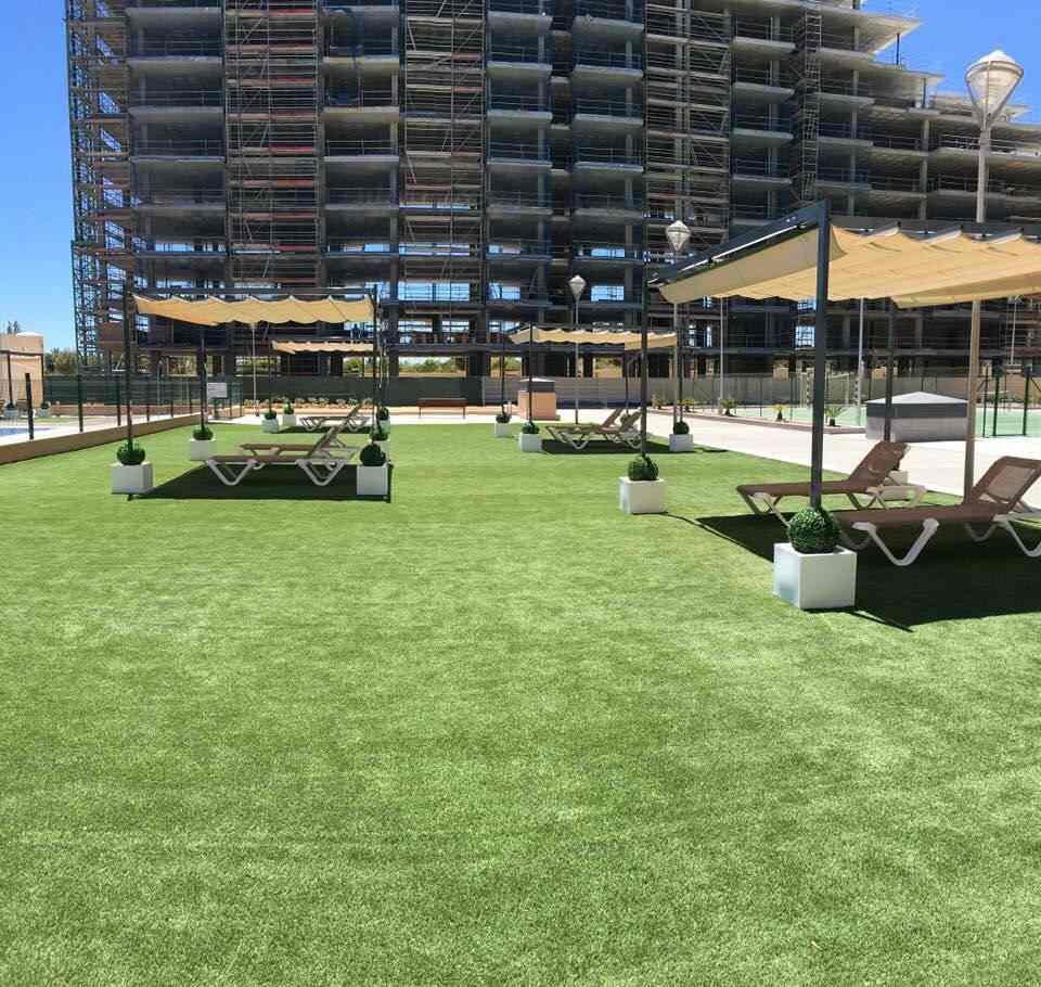 Un gran césped con sillas y sombrillas frente a un edificio en construcción.