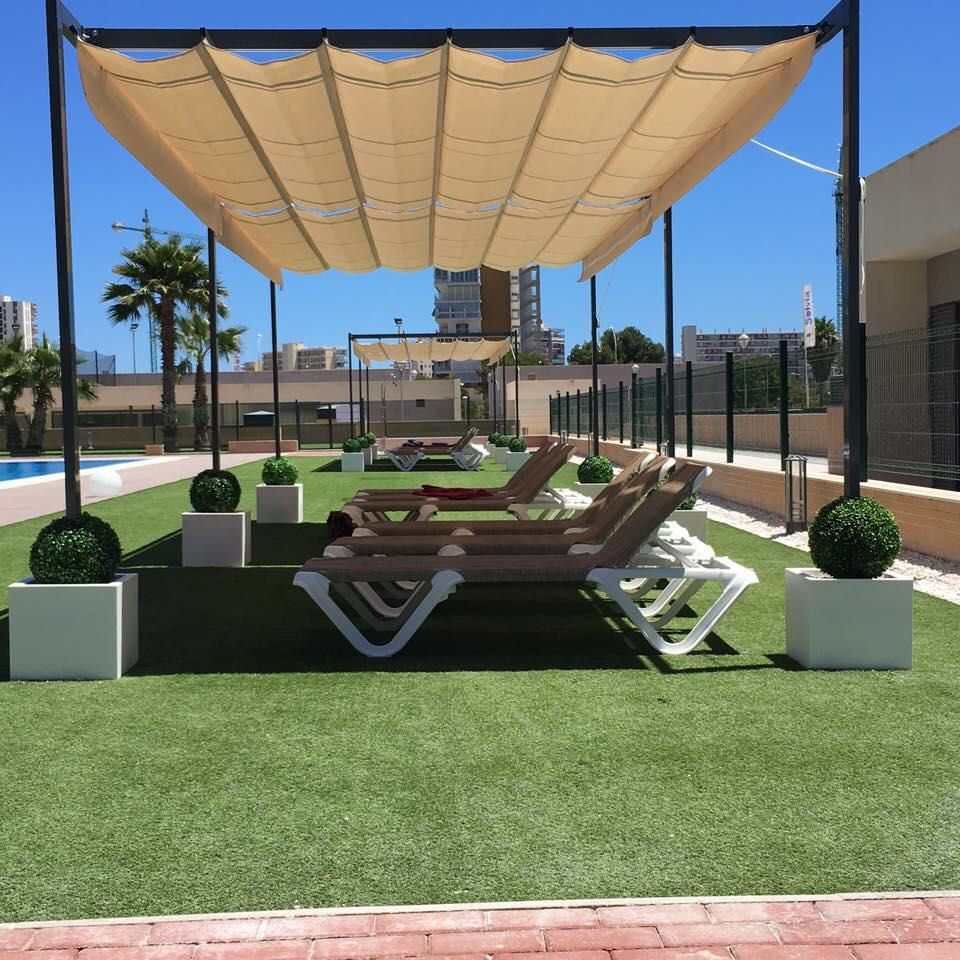 Una fila de sillas bajo un dosel con una piscina al fondo.