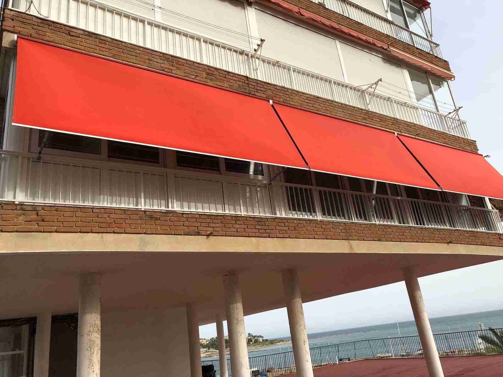 Un edificio con un toldo rojo en el balcón con vista al mar.
