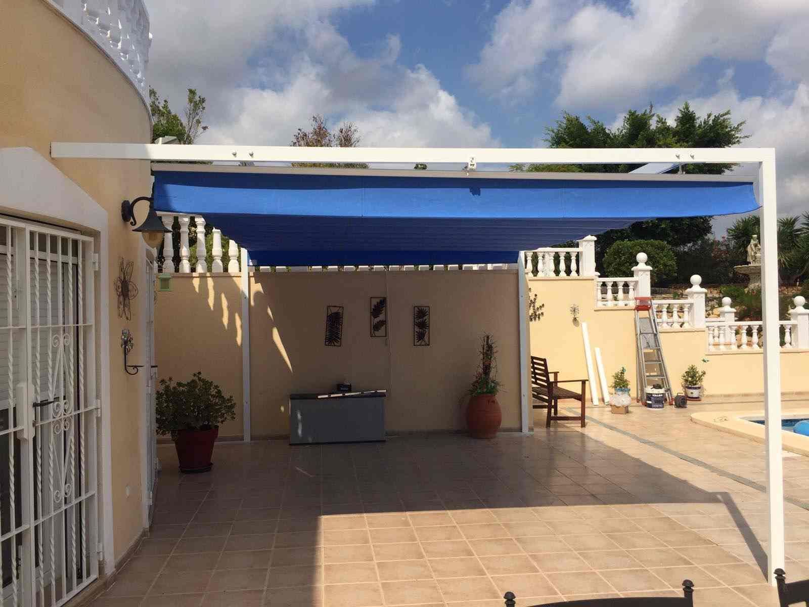 Un patio con un toldo azul encima y una piscina al fondo.