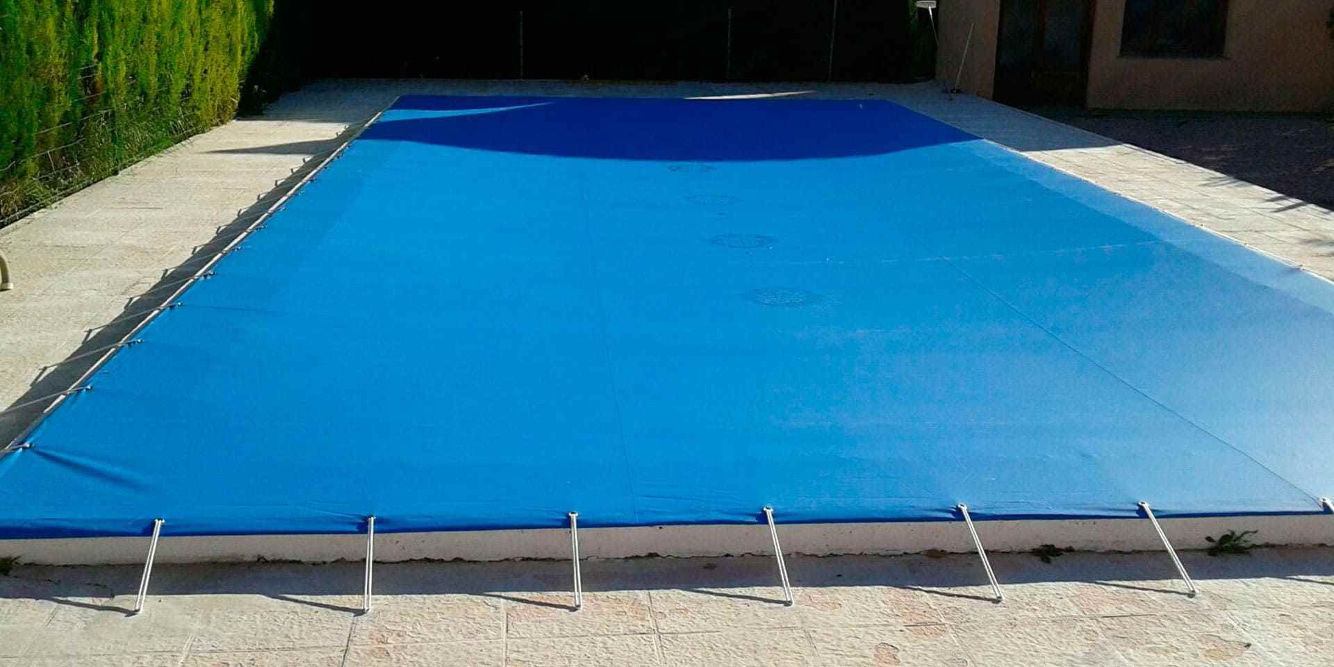 Cubierta de piscina azul sobre piscina rectangular, rodeada de patio de piedra.