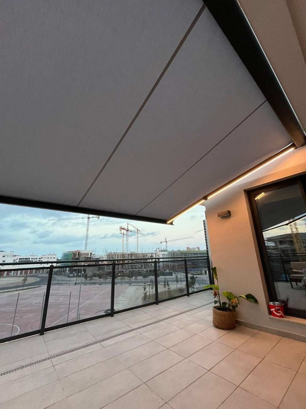 Balcón con toldo retráctil; barandilla de vidrio con vista a la ciudad con cielo nublado.