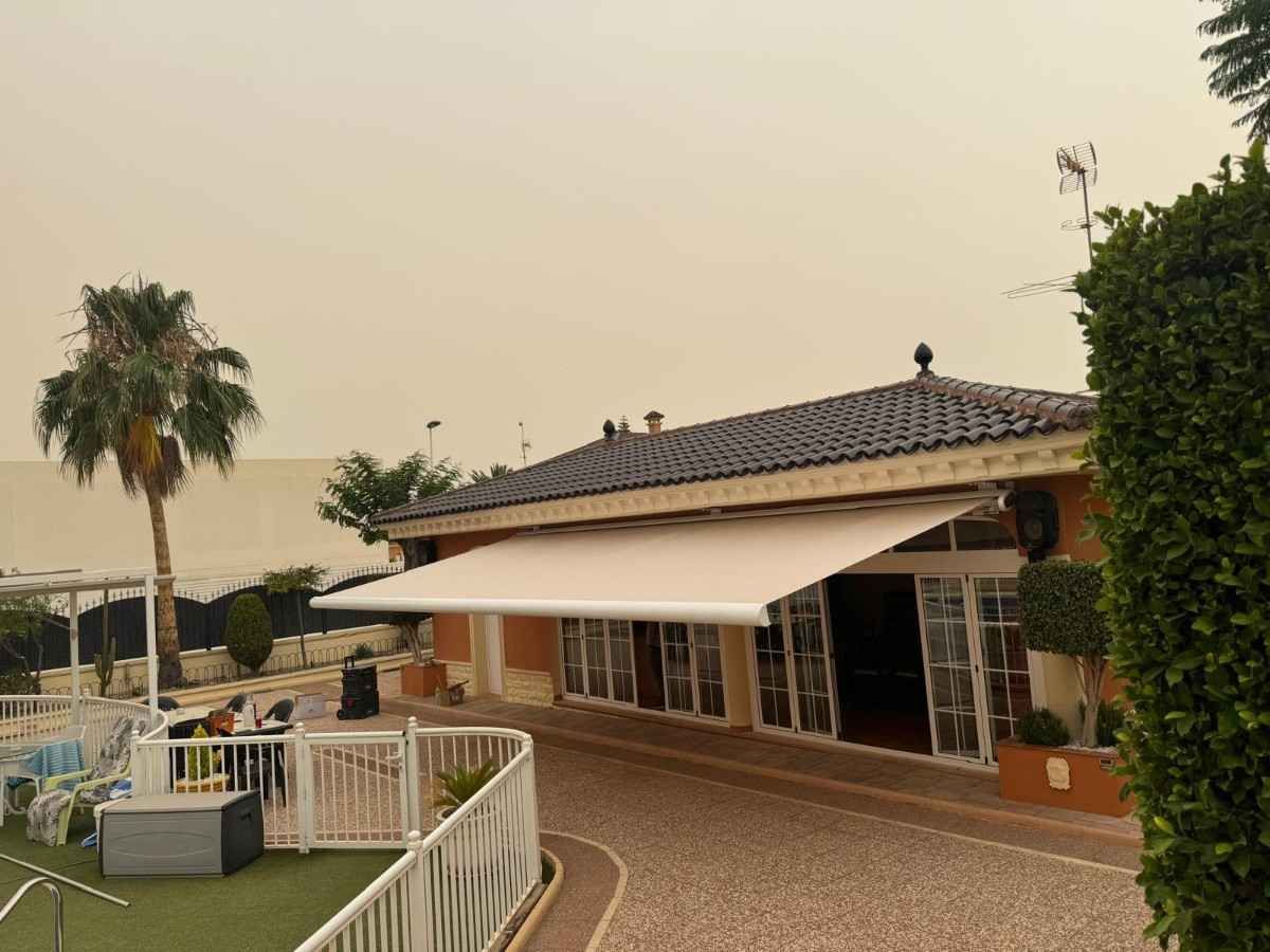 Letrero de la empresa Toldos Antón en un edificio con una puerta gris cerrada. El logotipo incluye formas rojas y grises.