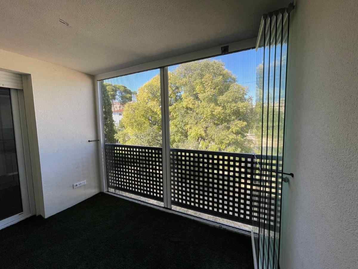 Balcón con mampara y barandilla de celosía. Árbol verde visible a través de la mampara y suelo de césped artificial.