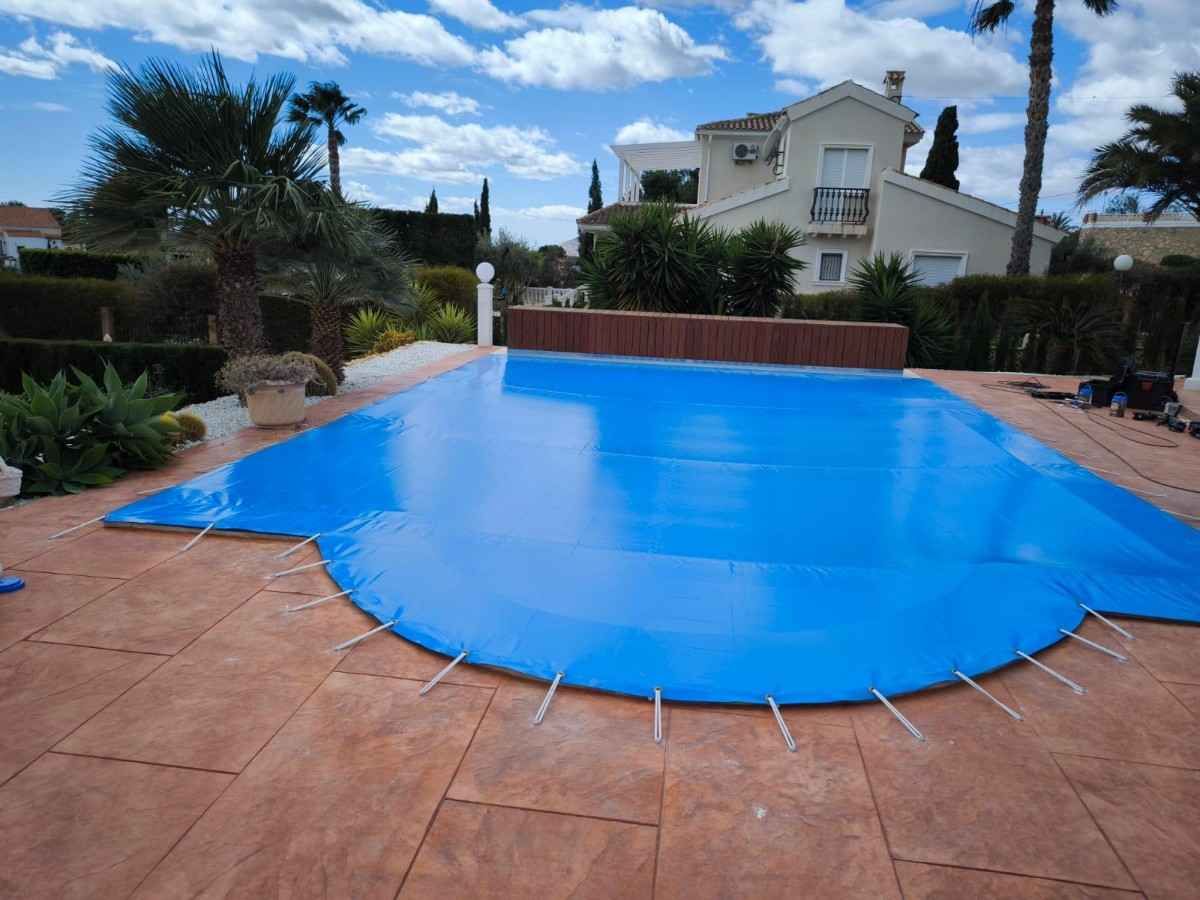 Cubierta azul para piscina rectangular exterior. La cubierta tiene aberturas circulares.