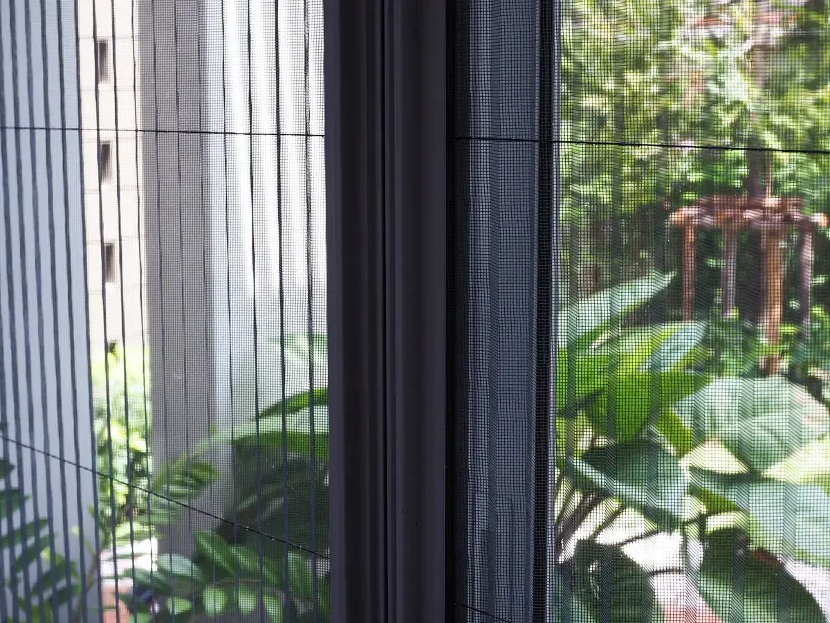 Ventana con mosquitera retráctil que deja ver una frondosa escena verde al aire libre.