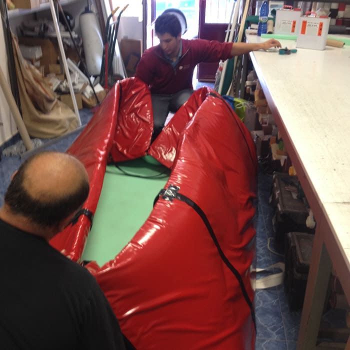 Dos hombres están trabajando en una canoa roja en un taller.
