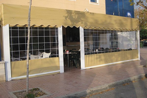 Cafetería con toldo color canela, ventanas y asientos al aire libre sobre una acera de ladrillo.
