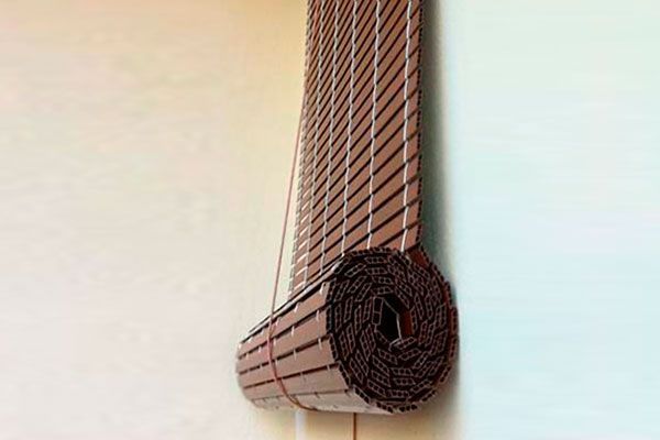 Un rollo de persianas de bambú cuelga en una pared blanca.