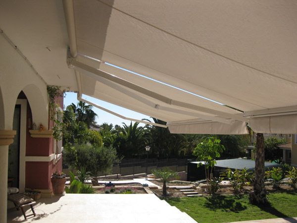 Un toldo blanco sobre un patio con vista a un jardín.