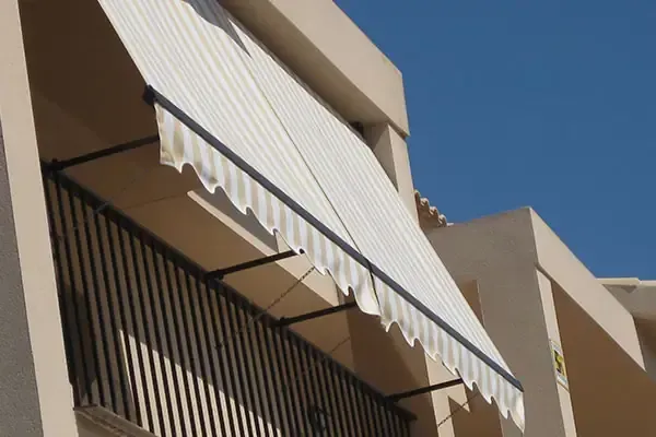 Un toldo de rayas beige y blancas se extiende sobre una barandilla de balcón negra.