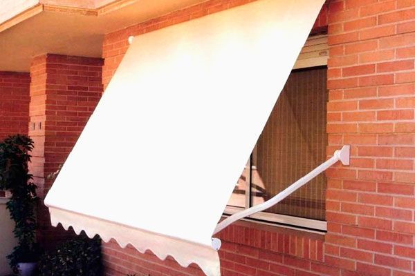 Un toldo blanco cuelga sobre una ventana de un edificio de ladrillo.