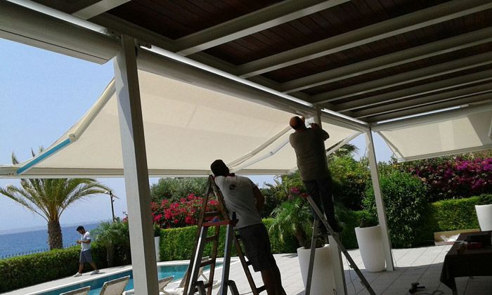 Dos hombres están trabajando en un toldo sobre una piscina.