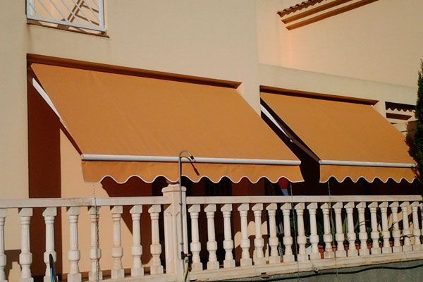 Un balcón con un toldo naranja y una barandilla blanca.
