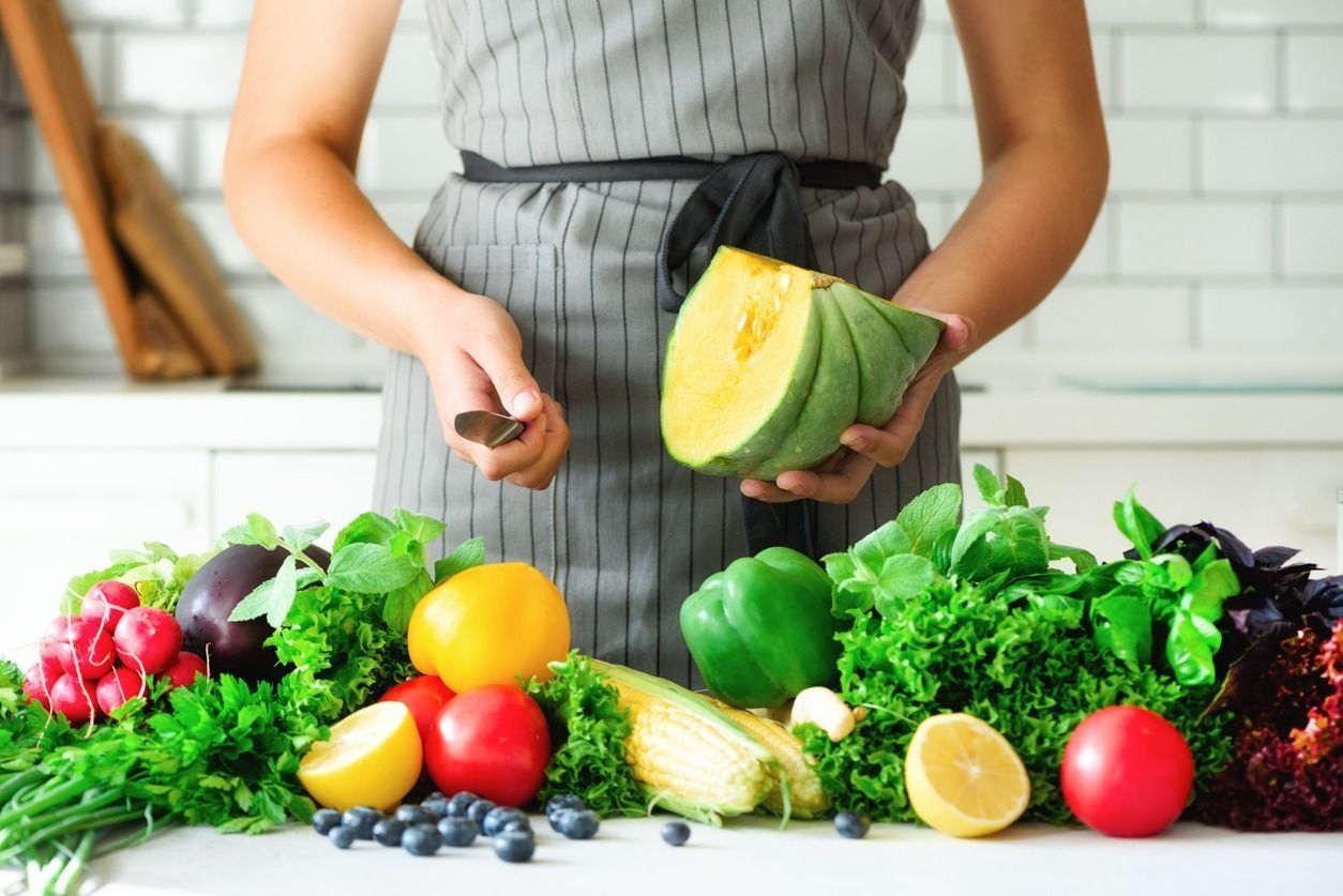 Una mujer está cortando verduras en una tabla de cortar en una cocina.