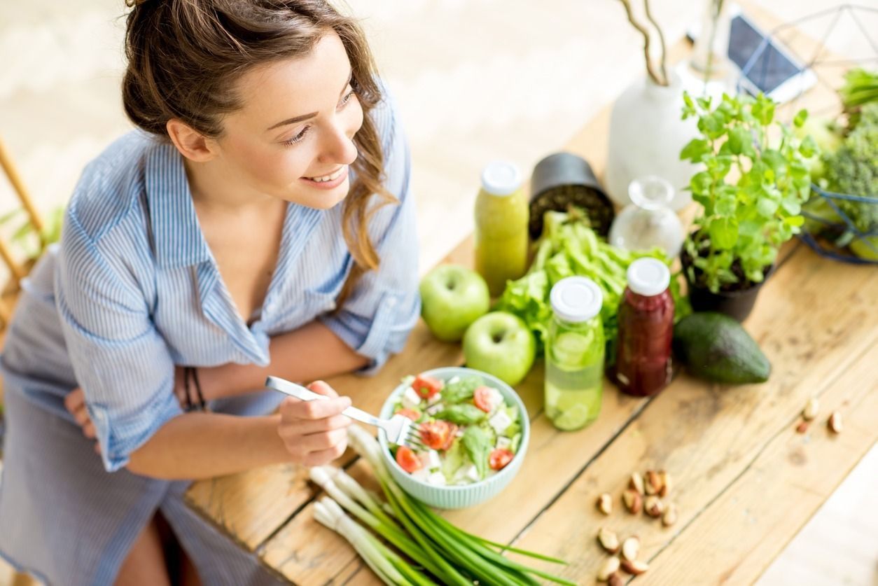 Una mujer está sentada en una mesa comiendo una ensalada.