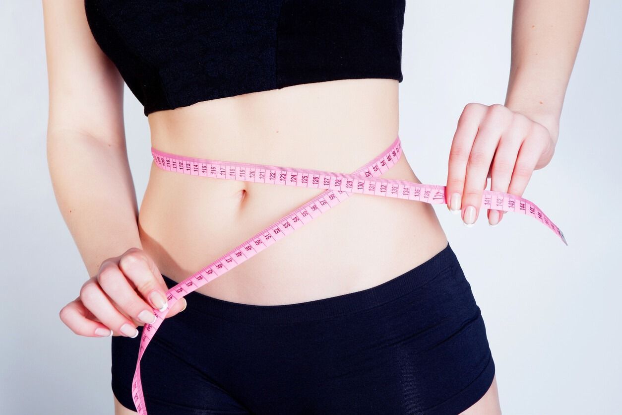 Una mujer está midiendo su cintura con una cinta métrica.
