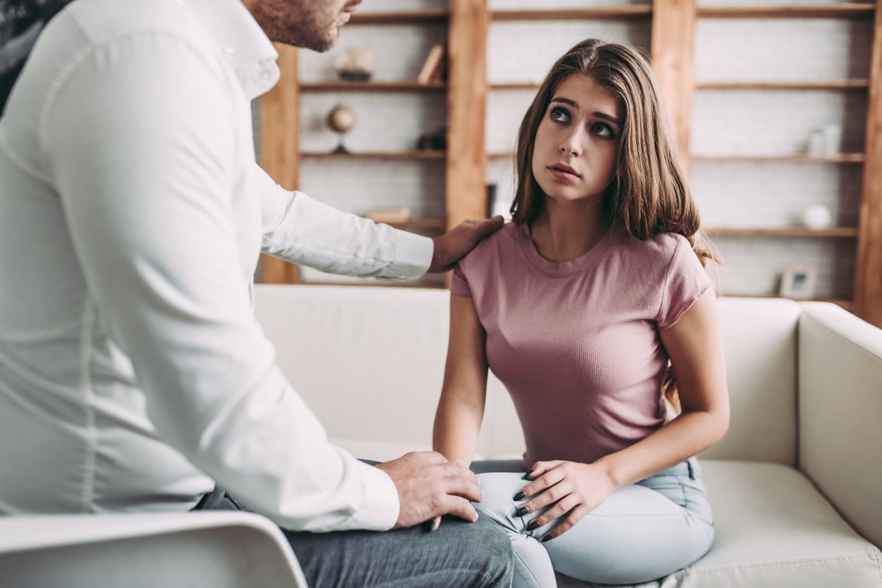 Un hombre está consolando a una mujer que está sentada en un sofá.