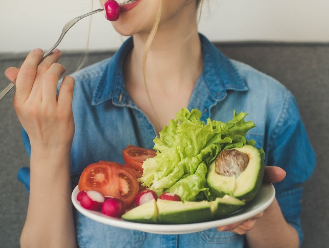 Una mujer está comiendo una ensalada con un tenedor de un plato.