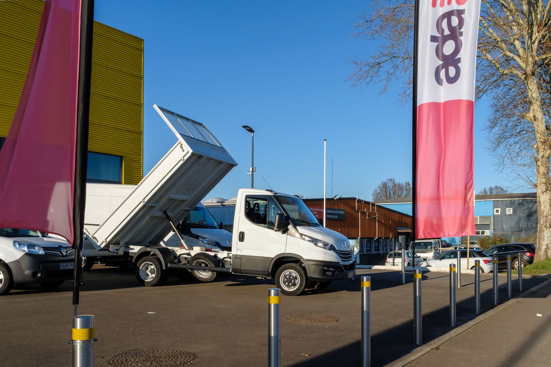 Plusieurs utilitaires garés sur un parking devant un grand bâtiment jaune.