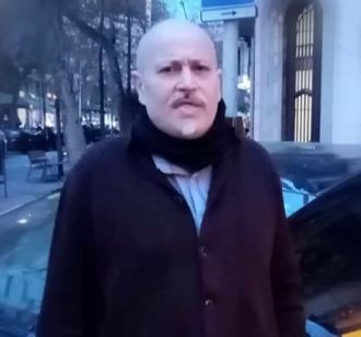 Un hombre calvo con bigote está parado frente a un automóvil.